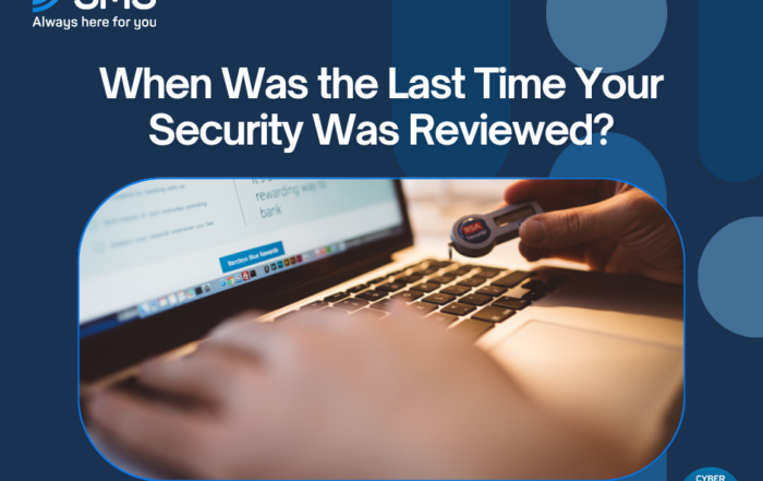 SMS branding and the headline 'When Was the Last Time Your Security Was Reviewed?' over a blue geometric background with a laptop and security key photo in a rounded frame, plus a Cyber Essentials badge in the corner.